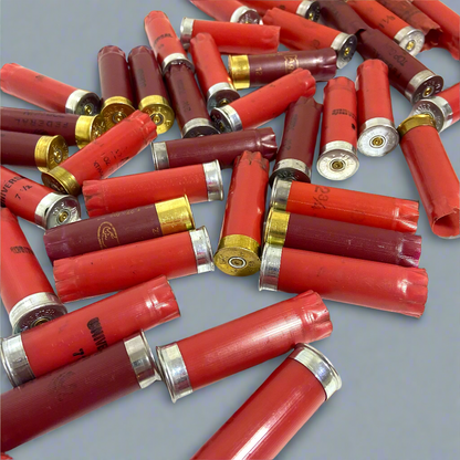 Scattered pile of mixed red and burgundy empty shotshells showing both silver and gold bases on a plain background.