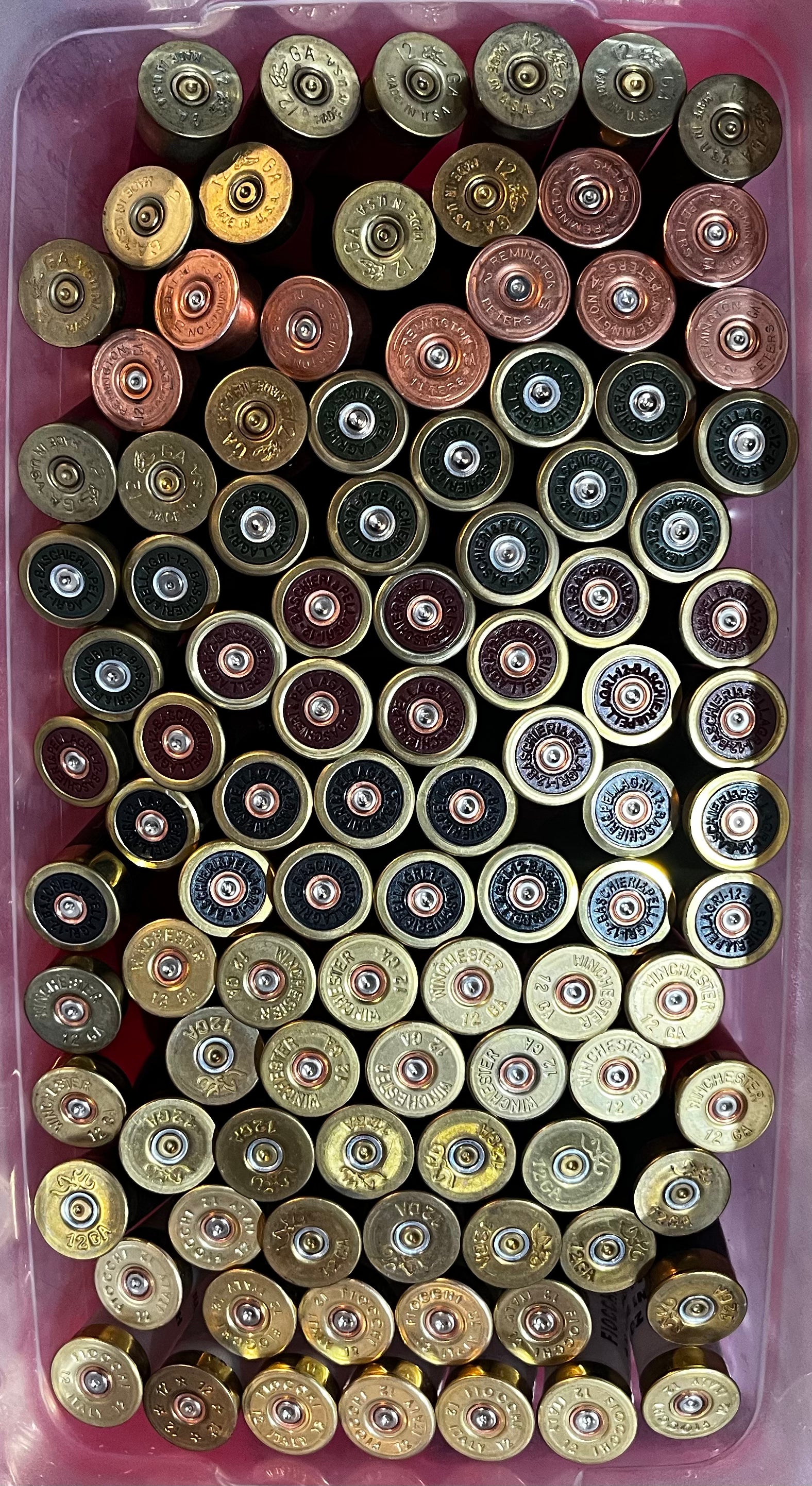 Bin filled with mixed shotgun shell brass bases in gold, copper, maroon, and black finishes, viewed from above