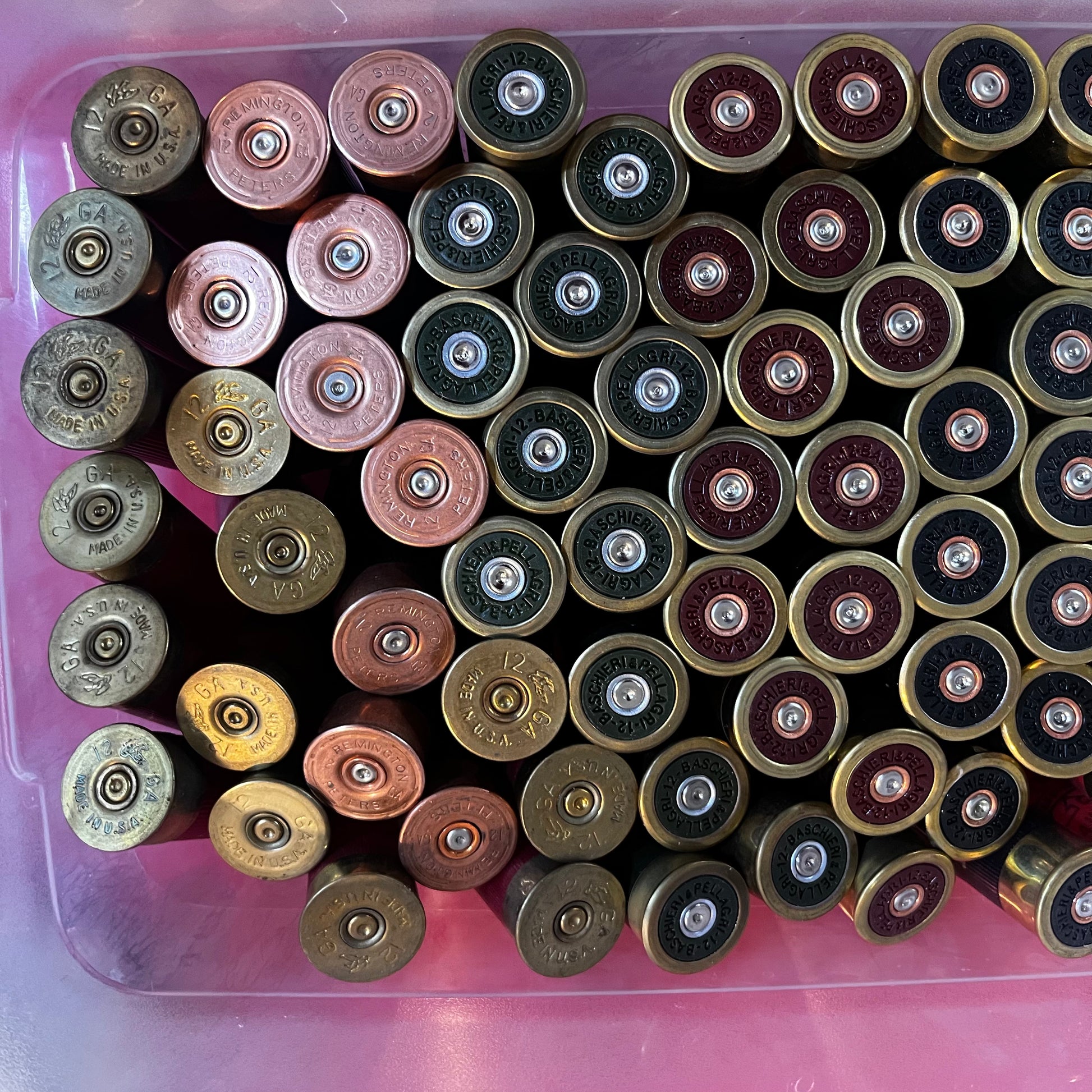 Bin filled with mixed shotgun shell brass bases in gold, copper, and maroon finishes with visible headstamps, viewed from above