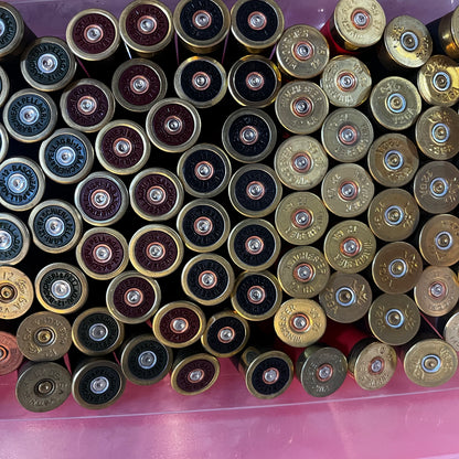 Bin filled with mixed shotgun shell brass bases in gold, copper, and dark finishes with visible headstamps, viewed from above