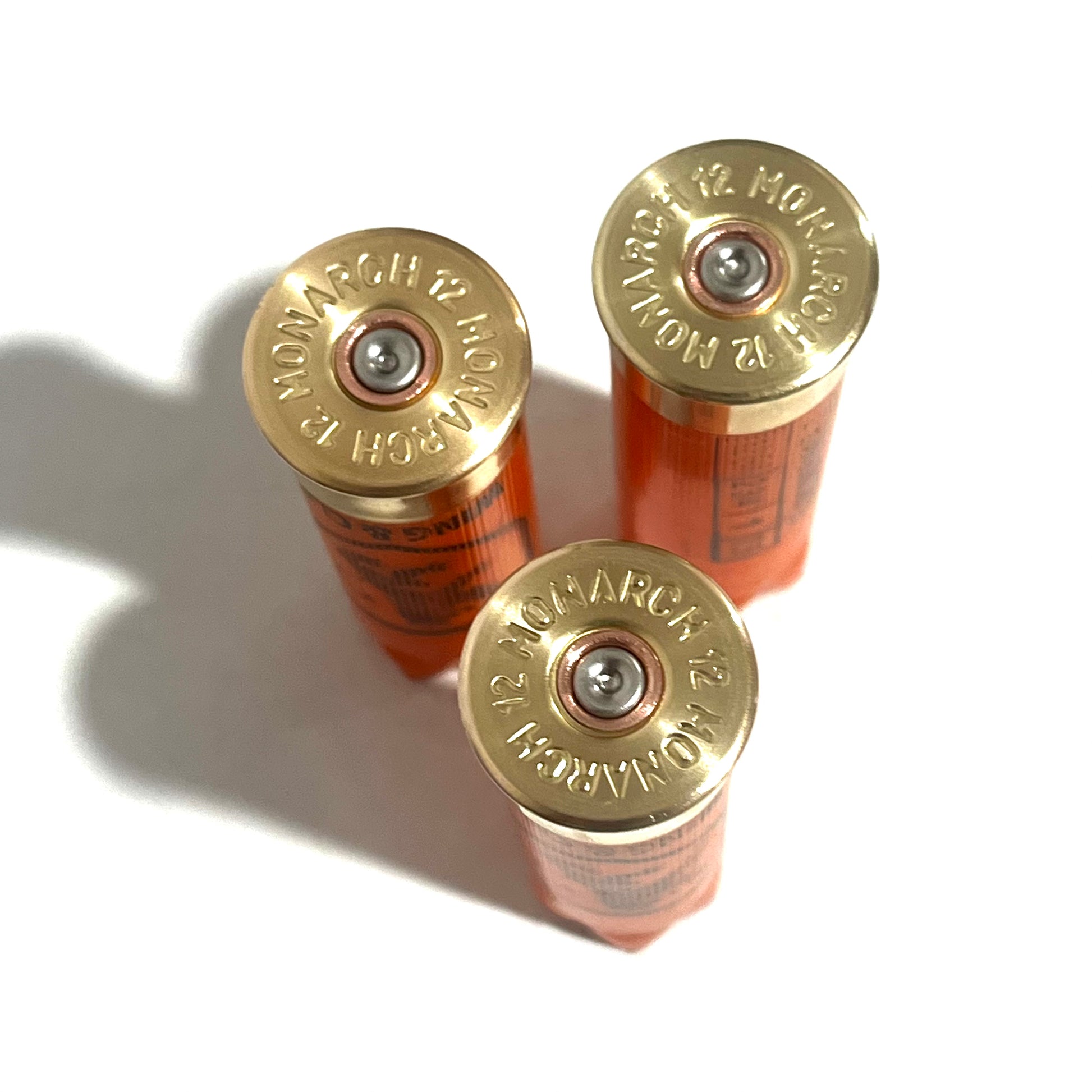 3 brass base caps of orange Monarch 12 gauge shotgun shells, viewed from above showing headstamps