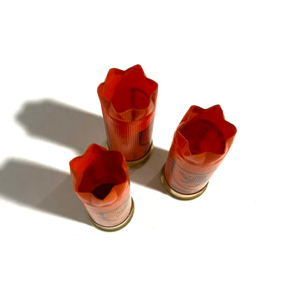 3 orange Monarch shotgun shells with star-fold crimped tops, viewed from above showing open mouths