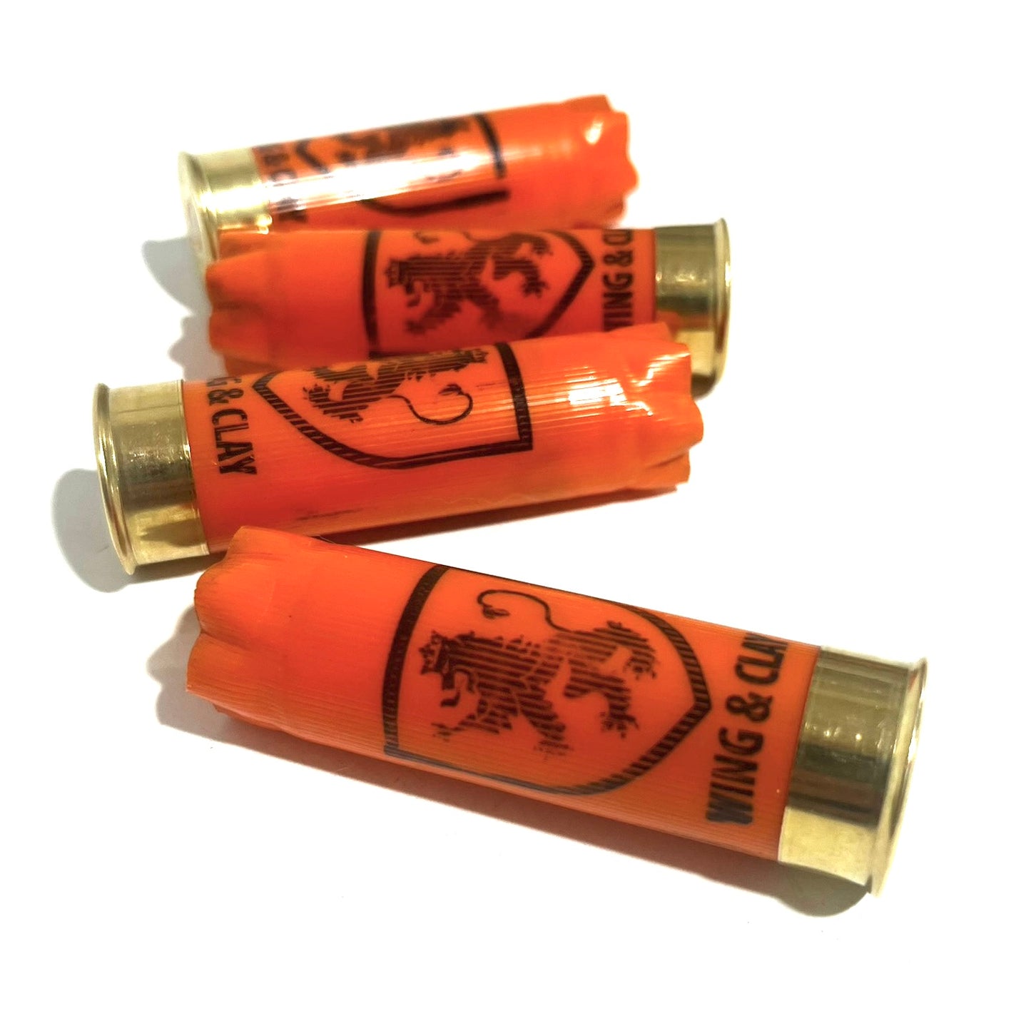 4 orange Monarch Wing & Clay 12 gauge shotgun shells with a lion crest logo, lying on a white background