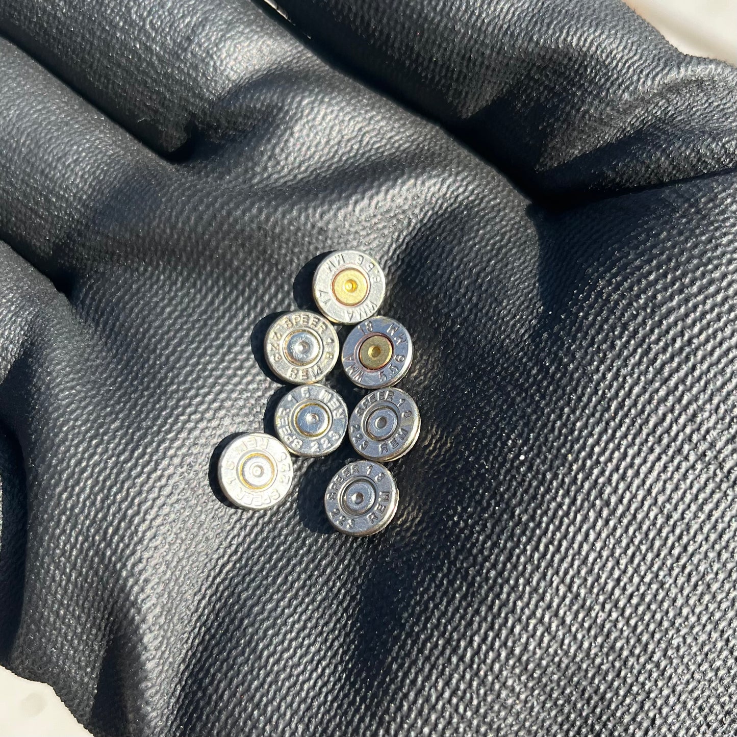 Seven polished nickel 223 5.56 bullet slices resting on a black fabric surface
