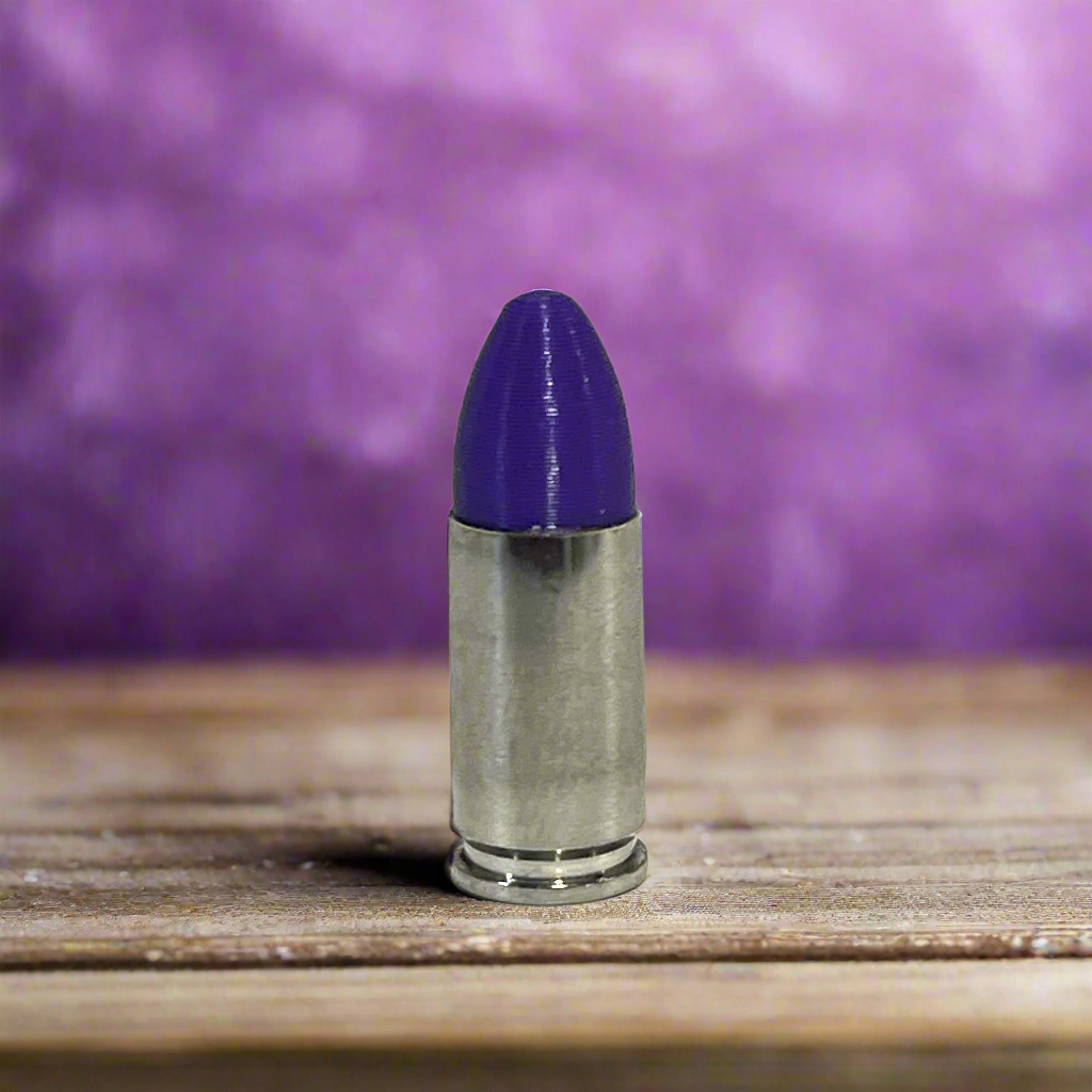A nickel 9mm Luger cartridge with a purple bullet tip standing on a wood surface against a purple background