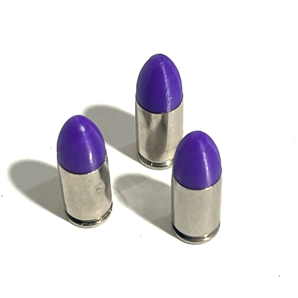 3 nickel 9mm Luger cartridges with purple bullet tips standing on a white background