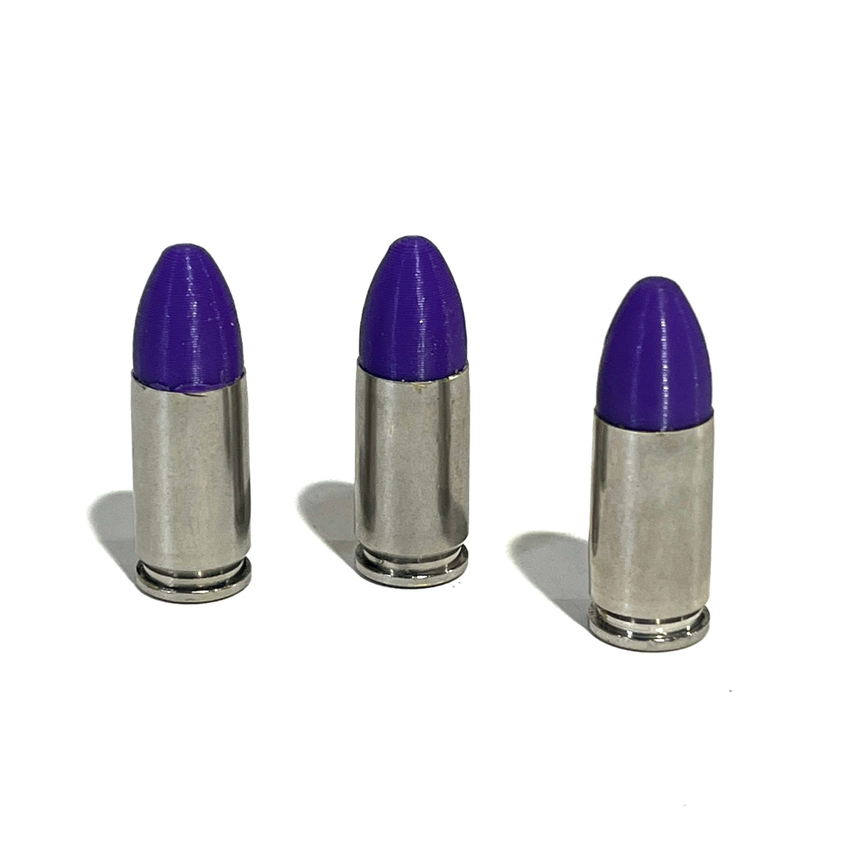 3 nickel 9mm Luger cartridges with purple bullet tips standing upright on a white background