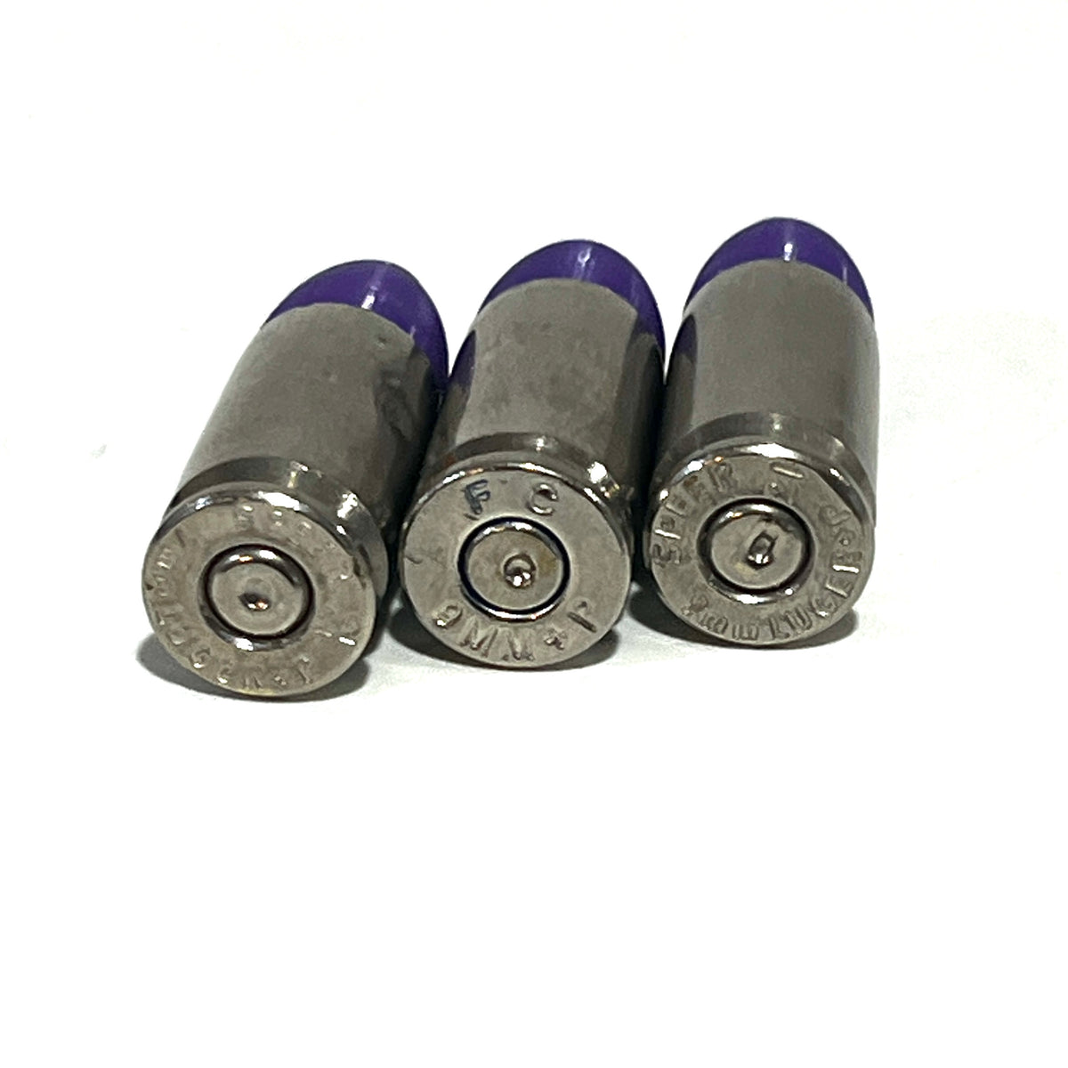 3 nickel 9mm Luger cartridges with purple tips viewed base first showing headstamps reading 9MM P and Luger