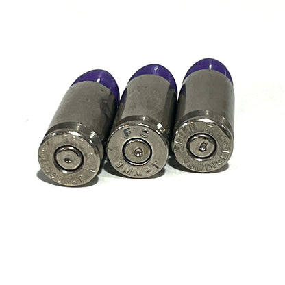 3 nickel 9mm Luger cartridges with purple tips viewed base first showing headstamps reading 9MM P and Luger