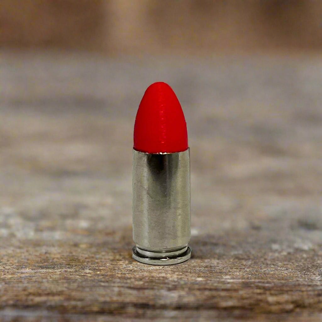 Single fake nickel 9mm Luger dummy round with red painted tip standing on weathered wood plank background