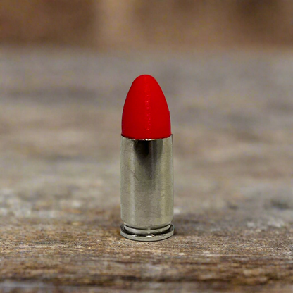 Single fake nickel 9mm Luger dummy round with red painted tip standing on weathered wood plank background
