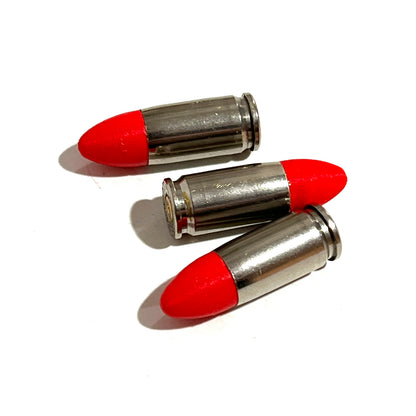 3 fake nickel 9mm Luger dummy rounds with red painted tips laid diagonally on white background