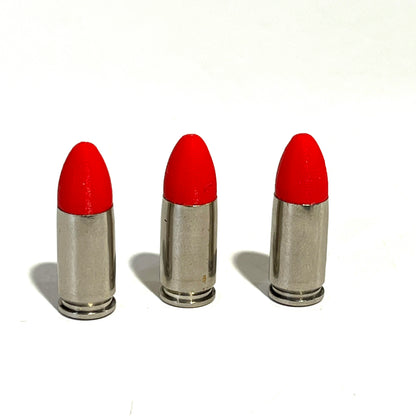 3 fake nickel 9mm Luger dummy rounds with red painted tips standing upright on a white background