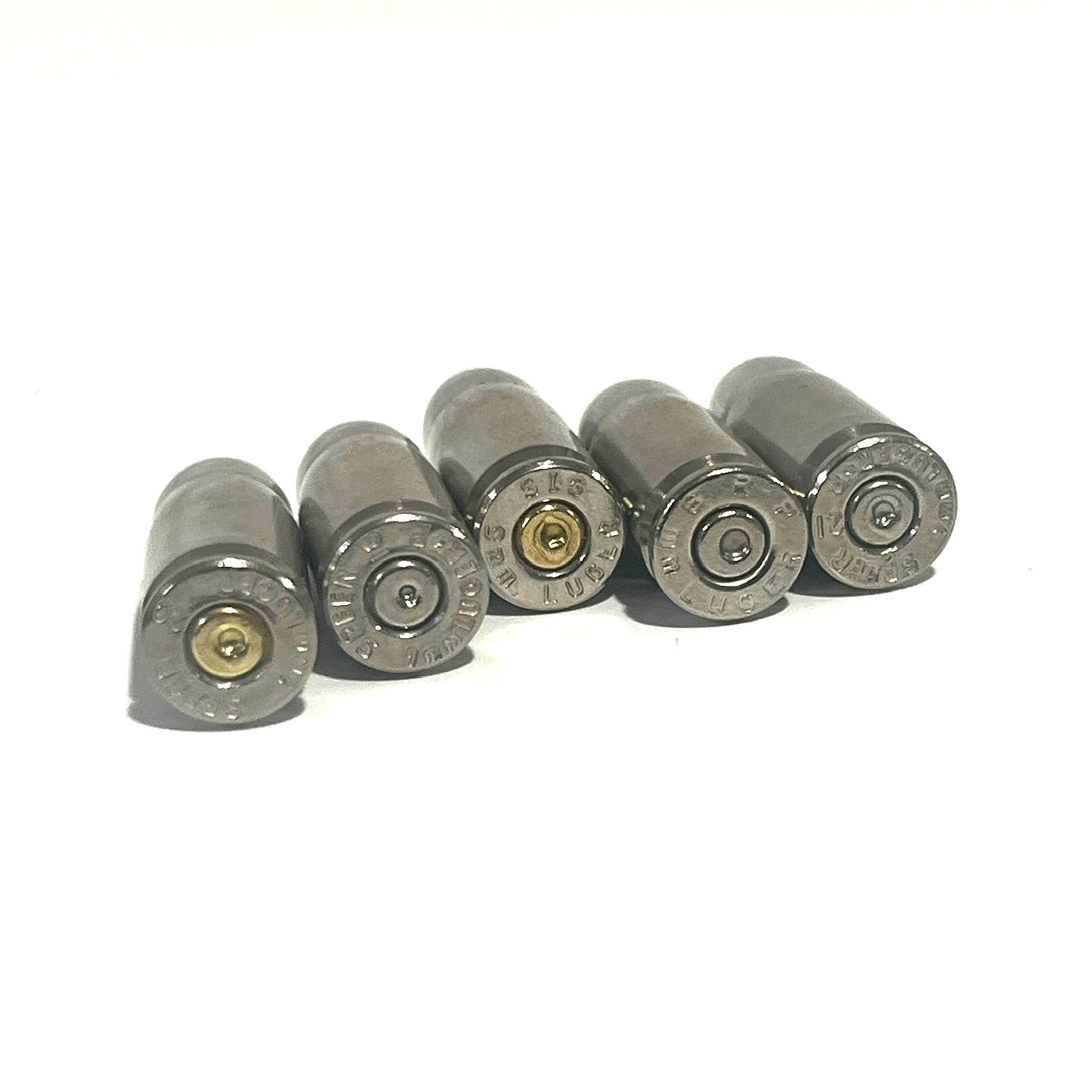 Five nickel 9mm Luger hulls lined up base-first, showing their stamped headstamps.
