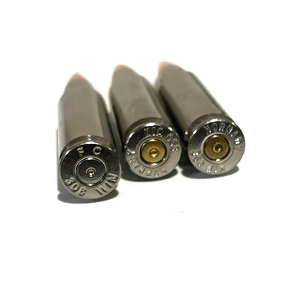 Three nickel .308 dummy cartridges base view showing an FC headstamp and varying primers