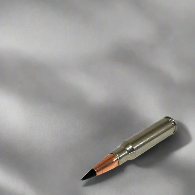 Single nickel .308 dummy round with black tip resting diagonally on a light gray fabric surface