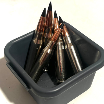 Several nickel .308 dummy rounds with black tips standing in a small gray plastic container