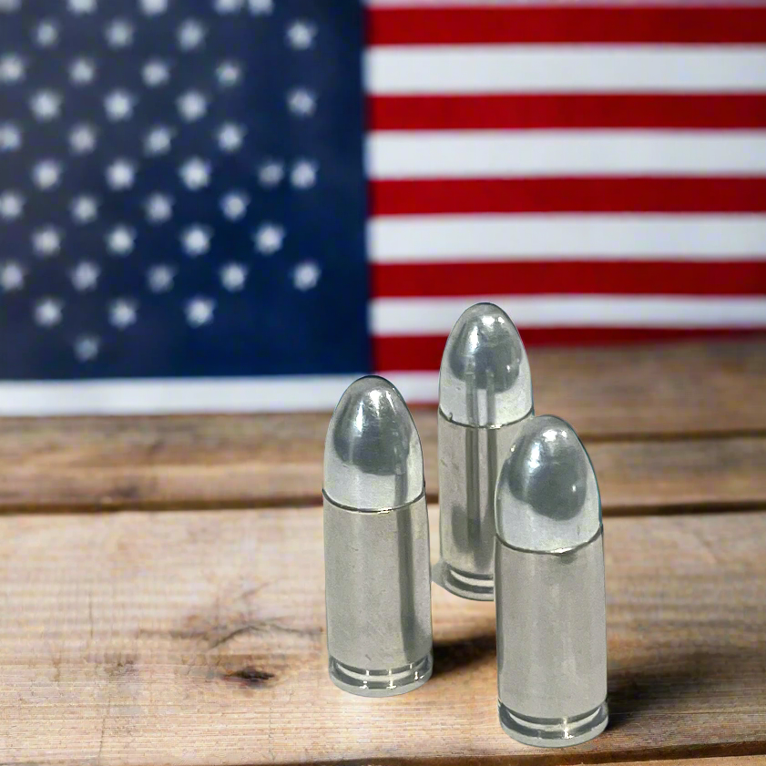 Three silver 9mm cartridges standing on a wood surface in front of an American flag.