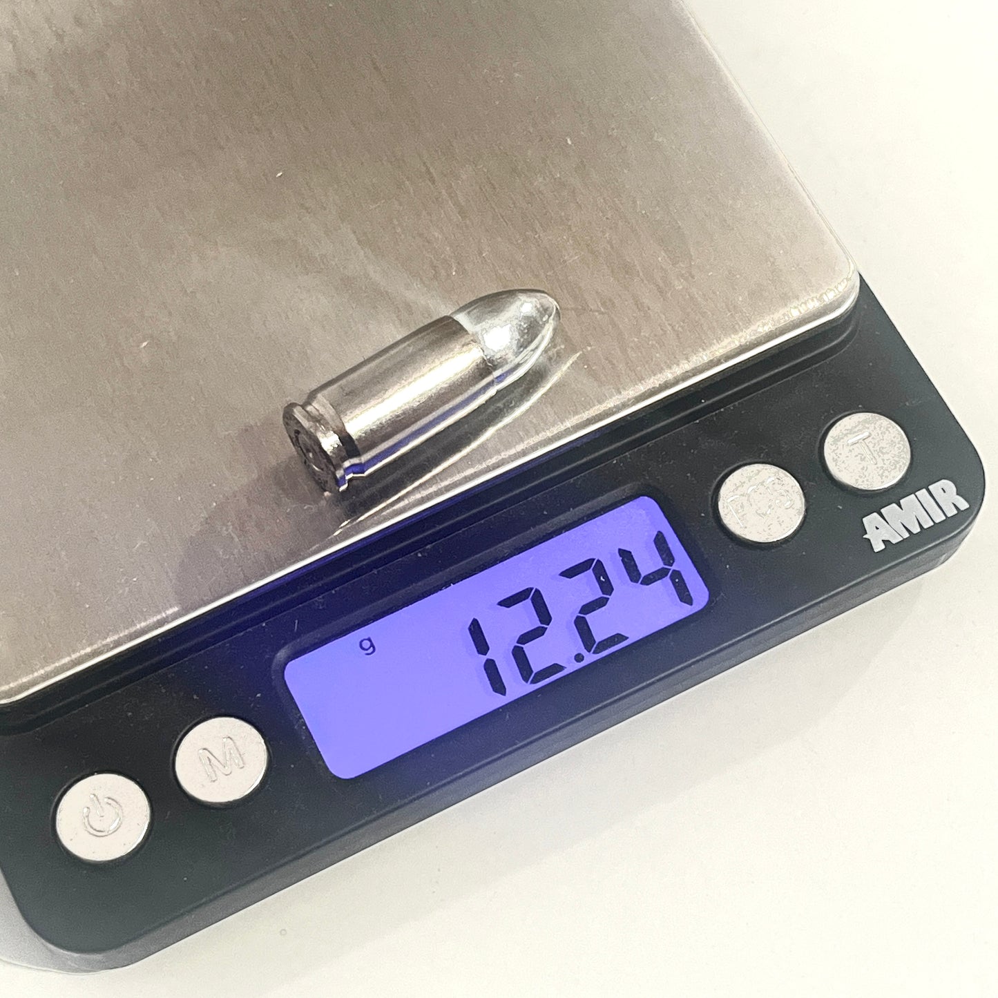 A nickel 9mm dummy round rests on a digital scale reading 12.24 grams.