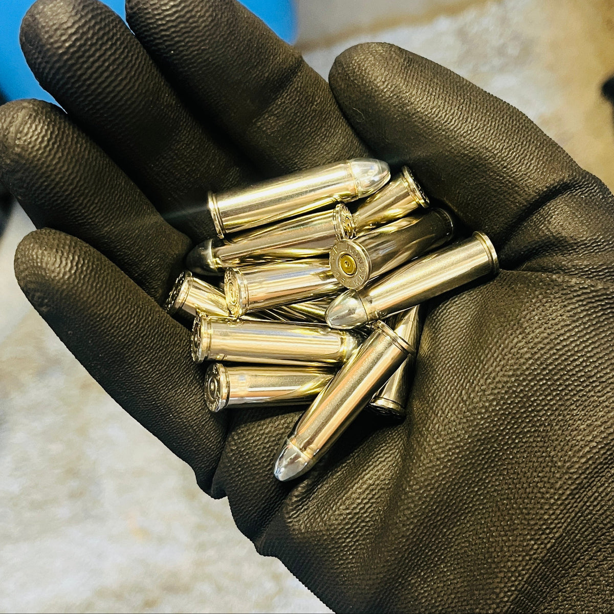 Handful of once-fired nickel 357 Magnum dummy rounds with round nose bullets held in a black gloved palm