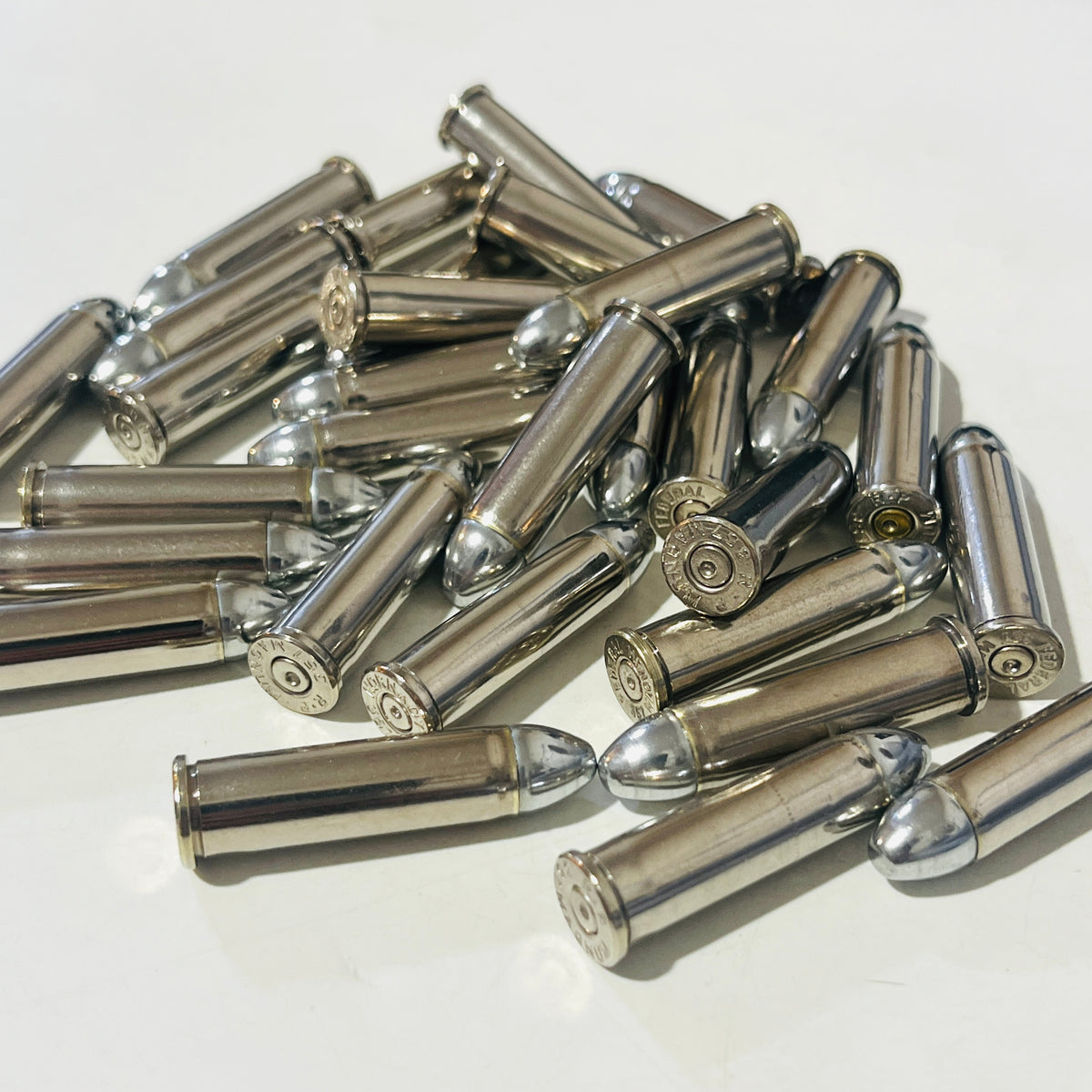 Overhead view of once-fired nickel 357 Magnum shells with round nose bullets scattered on a light surface