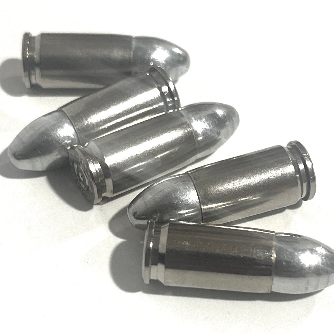 Five nickel 9mm shells fanned out on a white surface, one showing its base rim.
