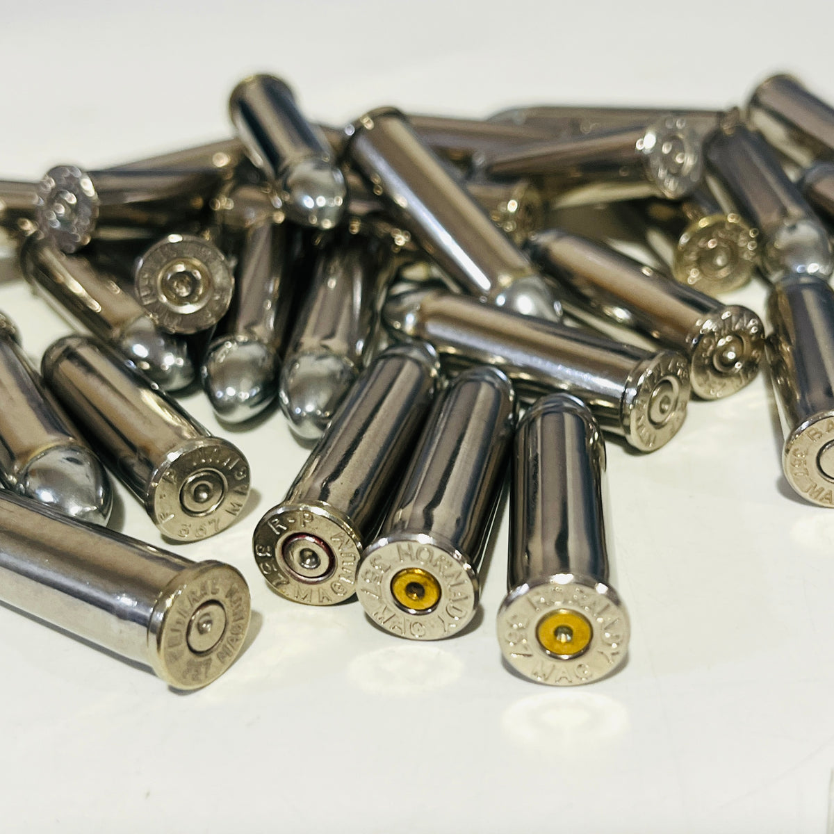 Close-up of used nickel 357 Magnum casings showing headstamps and spent primers, round nose bullets behind