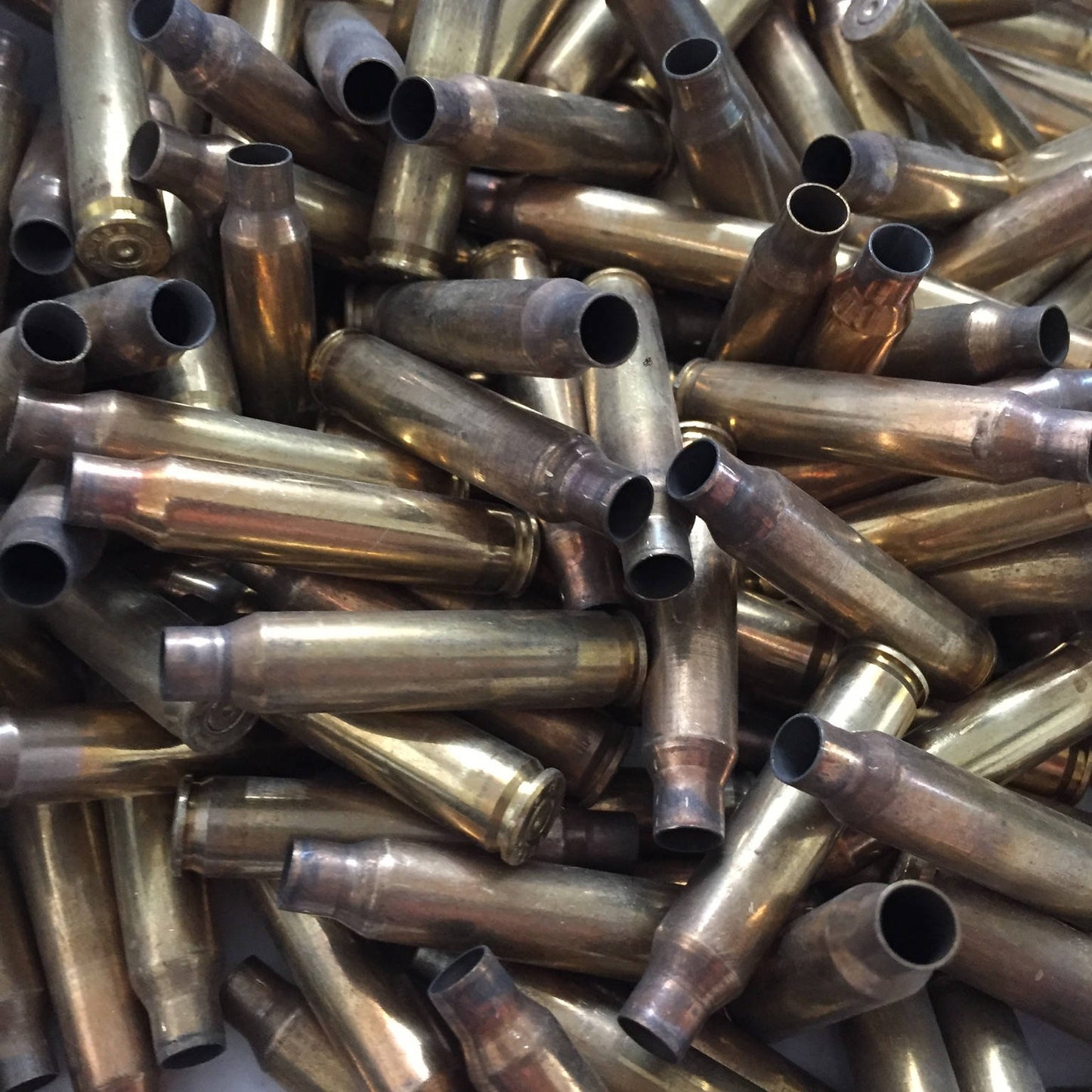 A dense, jumbled pile of uncleaned raw once-fired 5.56 brass rifle casings showing firing tarnish and neck wear.