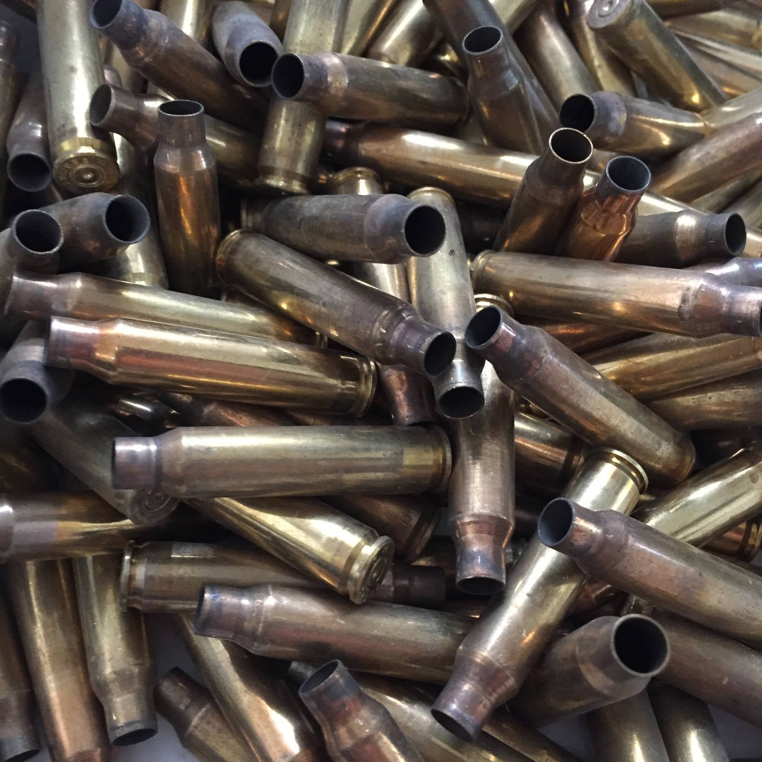 A dense, jumbled pile of uncleaned raw once-fired 5.56 brass rifle casings showing firing tarnish and neck wear.
