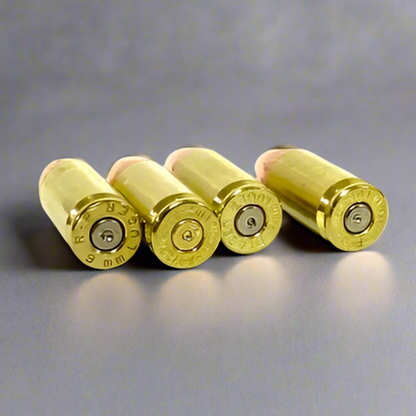 Four 9mm dummy rounds showing R-P, Winchester, A-Merc, and FC Luger headstamps on once-fired brass casings with dimpled inert primers.
