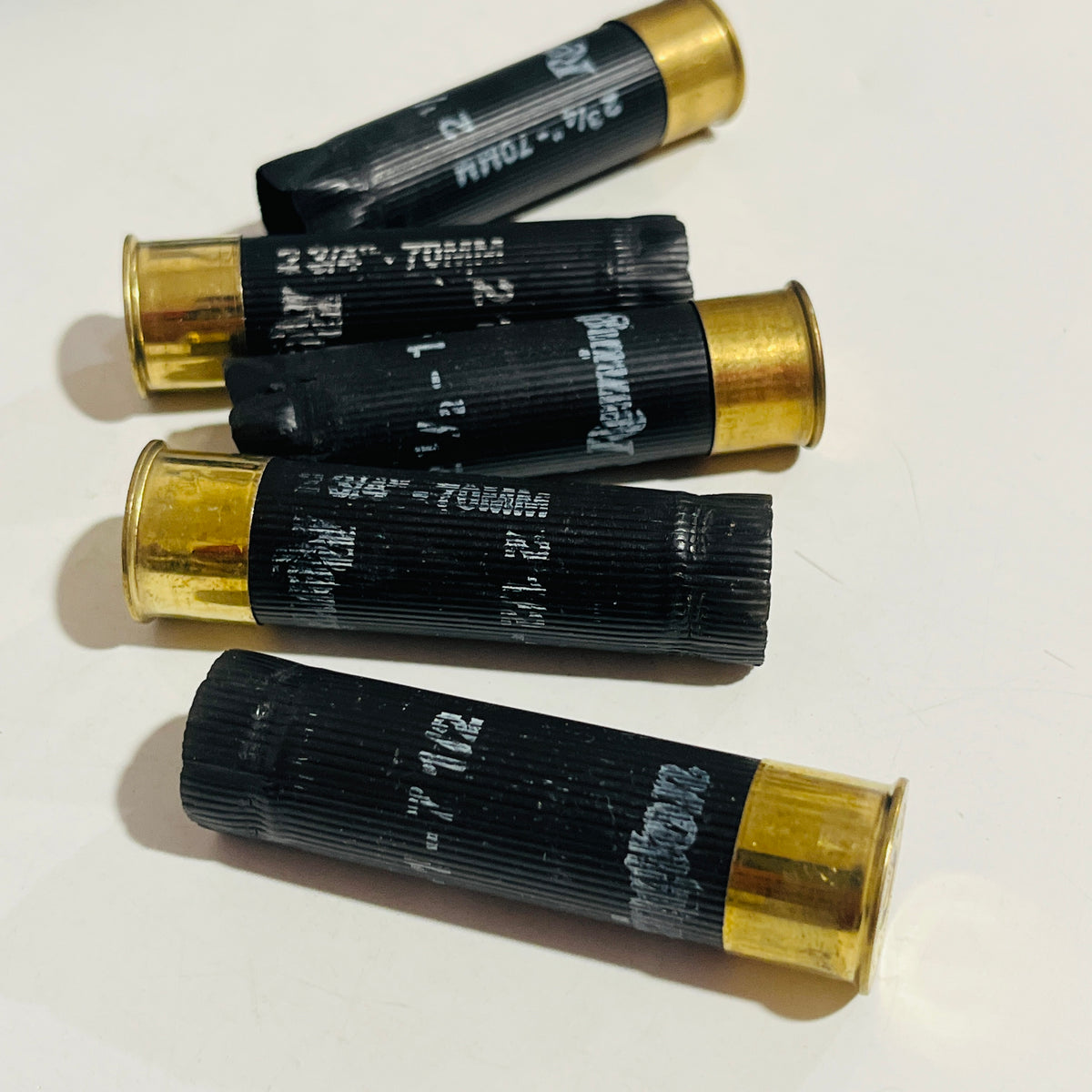 Five once-fired black shotgun casings with brass bases arranged in alternating directions on a white surface