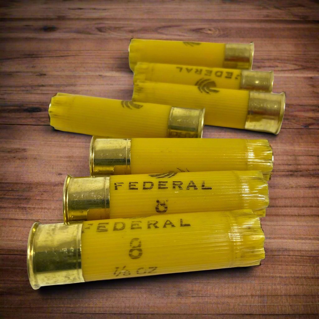Six yellow Federal brand shotgun shells arranged diagonally on a dark brown wood grain surface.