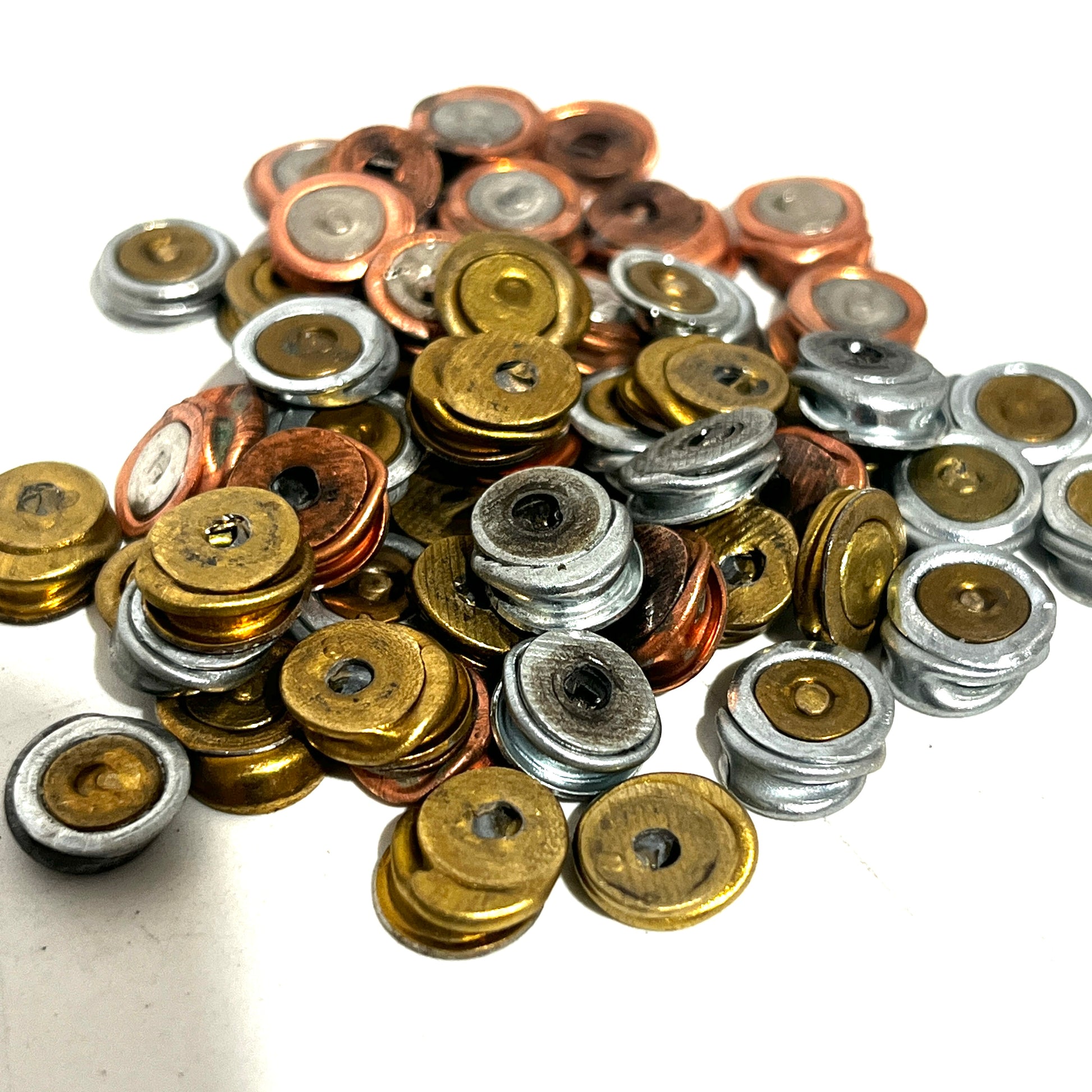A small loose pile of once fired primers showing individual metallic cups in brass, silver, and copper tones.