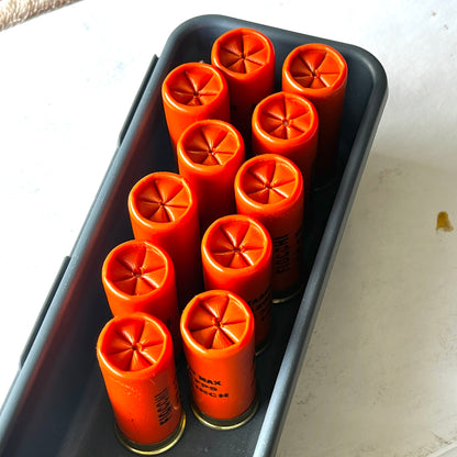 Ten orange empty dummy rounds standing crimped-end up in a black tray on a white surface.