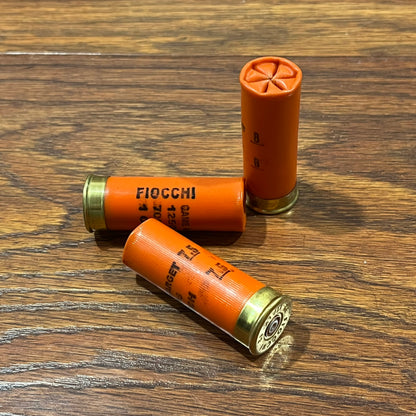 Three once-fired orange Fiocchi dummy rounds on a wood surface, one standing upright.