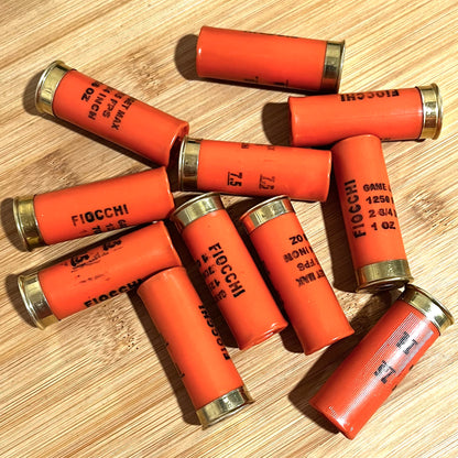 Ten spent orange Fiocchi hulls scattered on a wooden surface, showing Game & Target markings.
