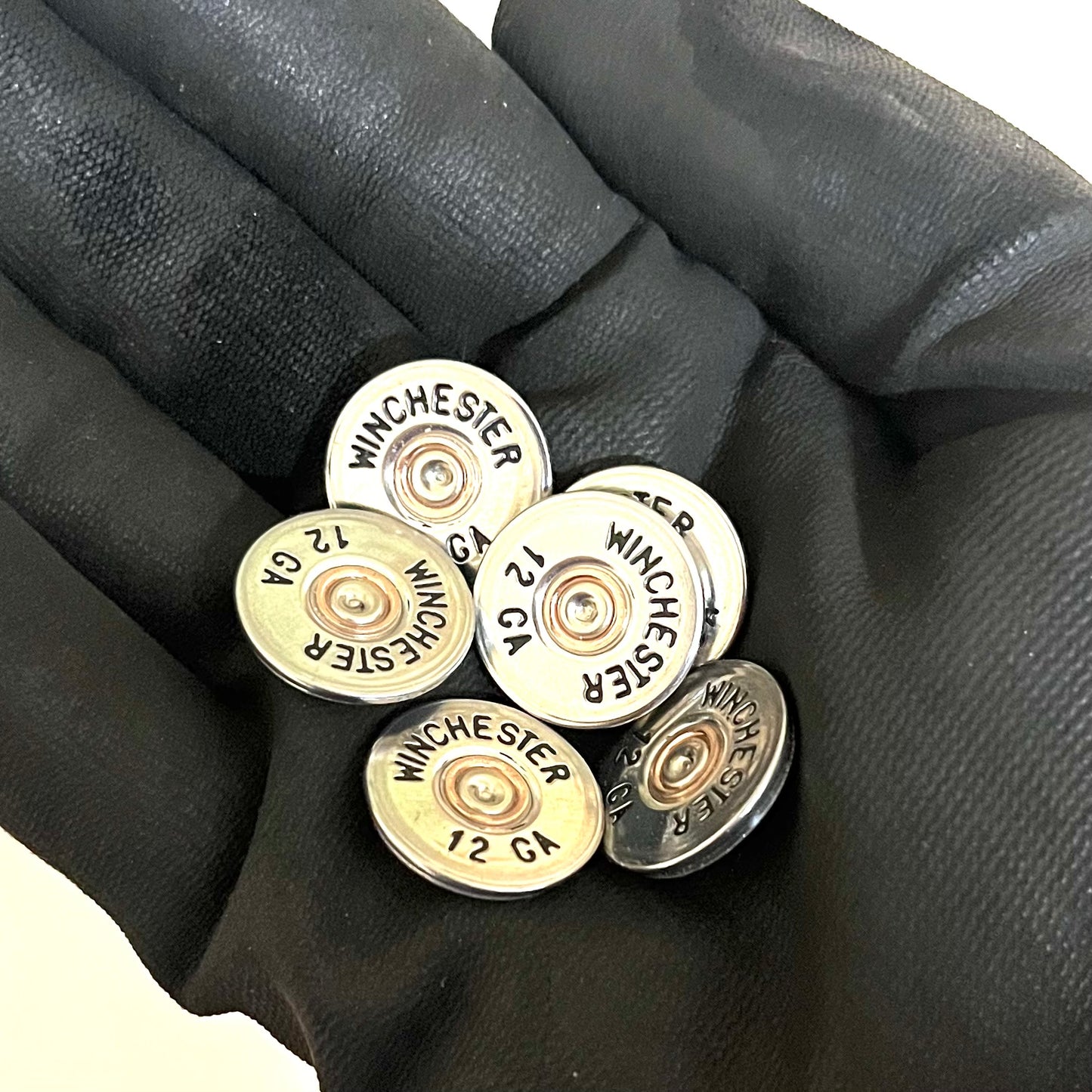 A handful of silver painted Winchester 12 gauge cut slices held in a black gloved hand.
