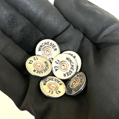 A handful of silver painted Winchester 12 gauge cut slices held in a black gloved hand.