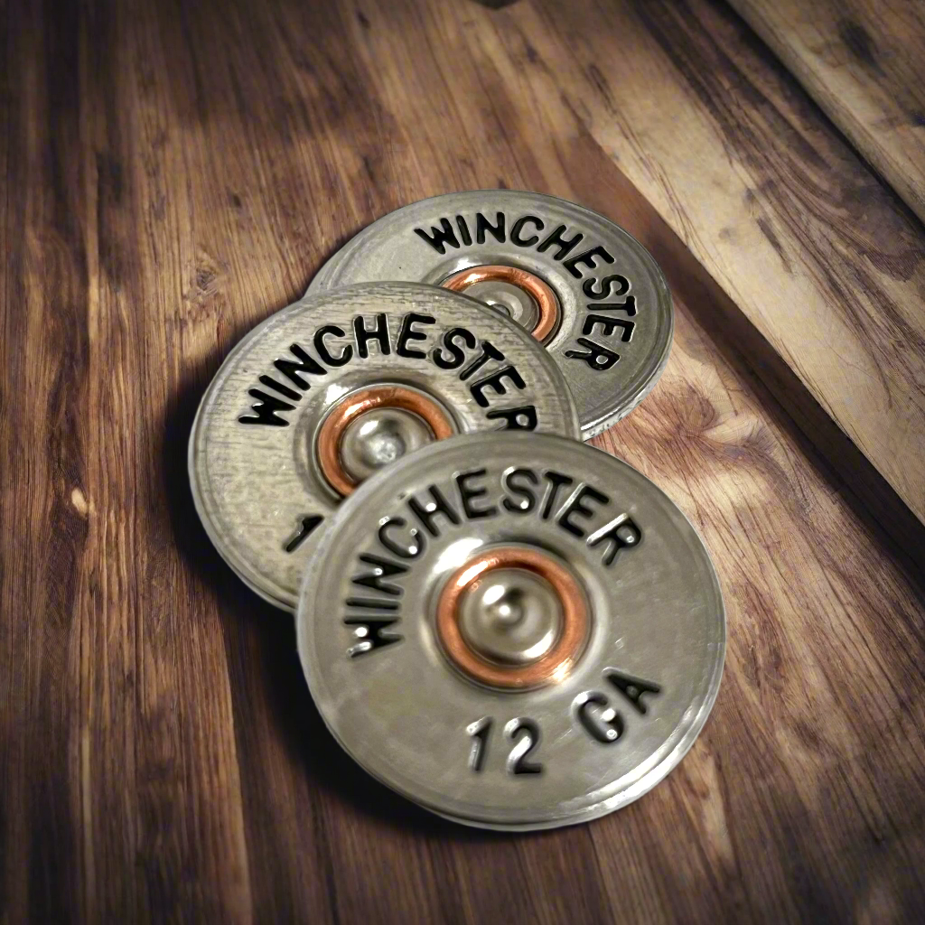 Three silver painted Winchester 12 gauge shotgun shell slices fanned out on a wood grain surface.