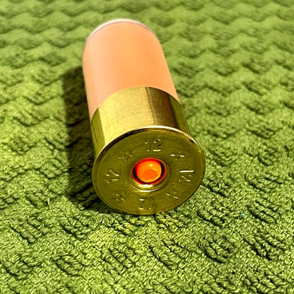 Peach mini shotgun shell brass base viewed from below showing 12 gauge headstamp and red primer, on green towel