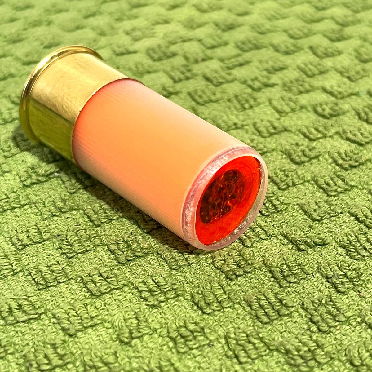 Peach mini shotgun shell with brass base laid on its side on green textured towel, red interior visible at open end