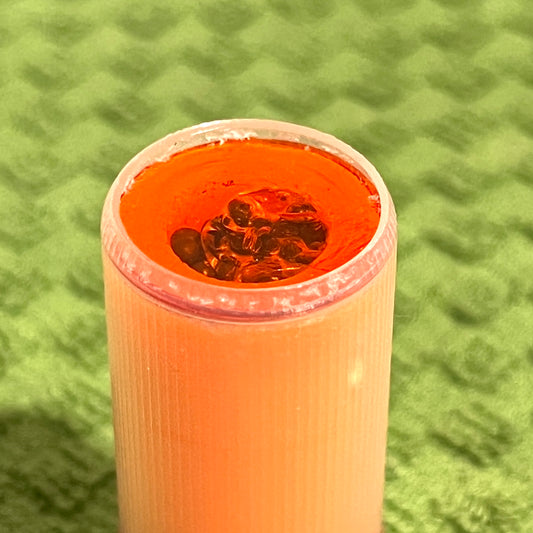 Close-up of peach mini shotgun shell open end showing red interior and dark wadding material, on green textured towel