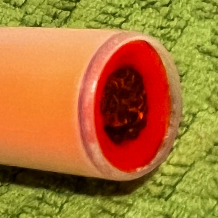 Extreme close-up of peach mini shotgun shell open end showing red interior and dark wadding material on green towel