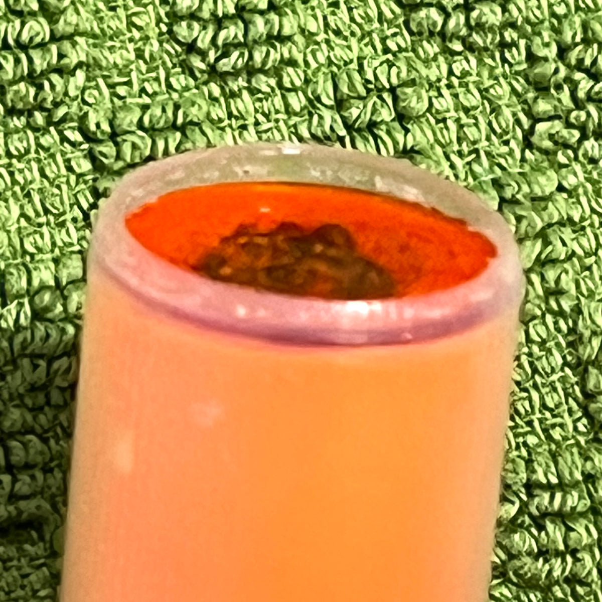 Peach mini shotgun shell open end viewed from above showing red interior and wadding, on green textured towel
