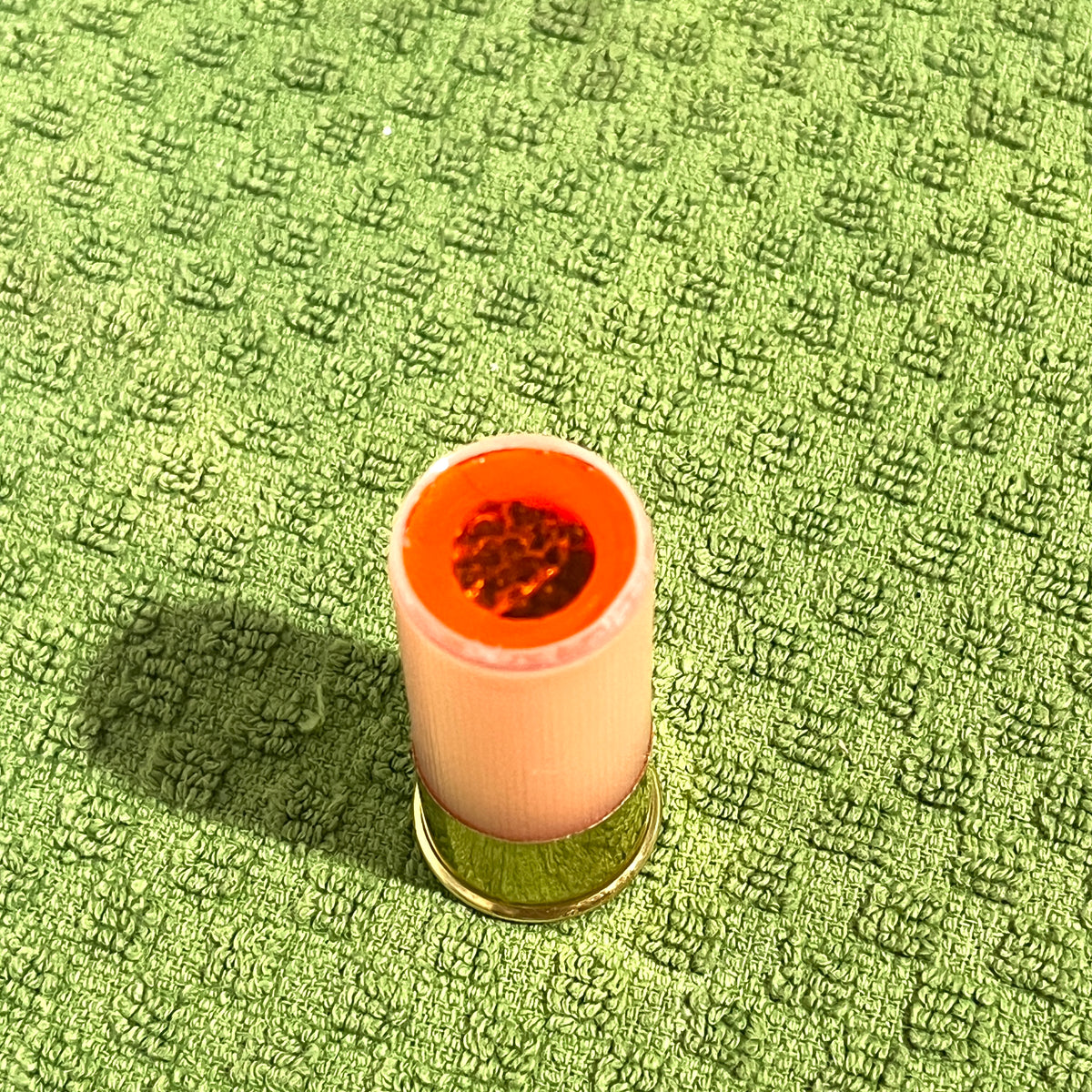 Peach mini shotgun shell standing upright on green textured towel, red interior visible at open top, brass base at bottom