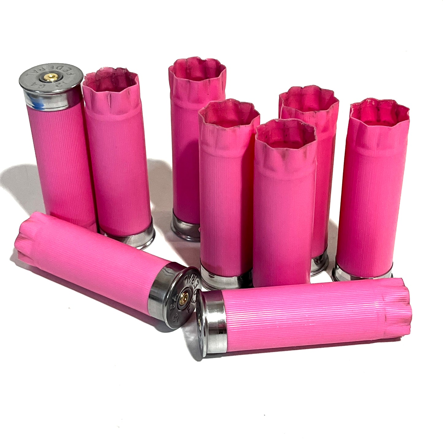 Eight pink 12 gauge blank shotgun shells with silver bases standing upright and lying on a white background