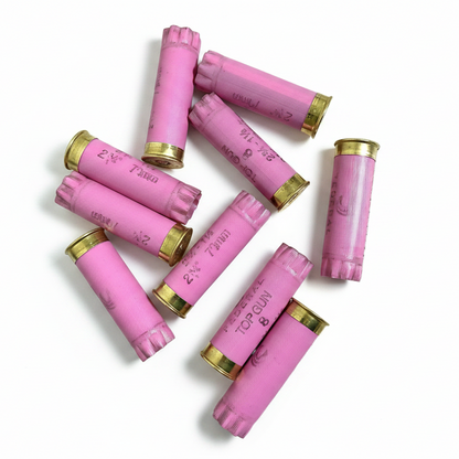 Nine pink Federal Top Gun casings scattered on a white wood plank background, showing brass bases.
