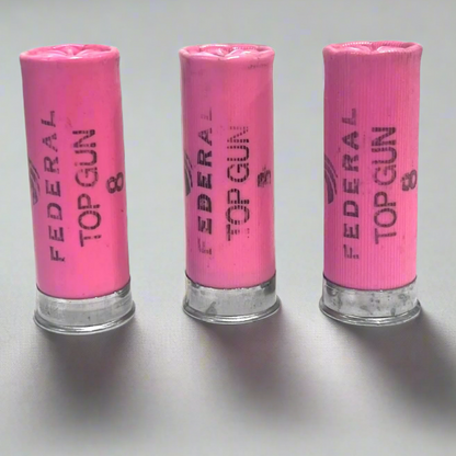 Three pink Federal Top Gun 8 shotgun shells standing on a gray surface with silver brass bottoms
