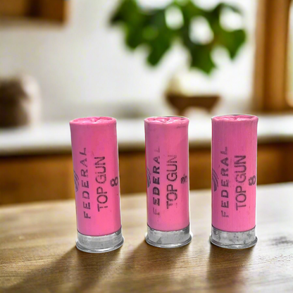 Three pink Federal Top Gun 8 shotgun shells standing on a wood table with a blurred kitchen background