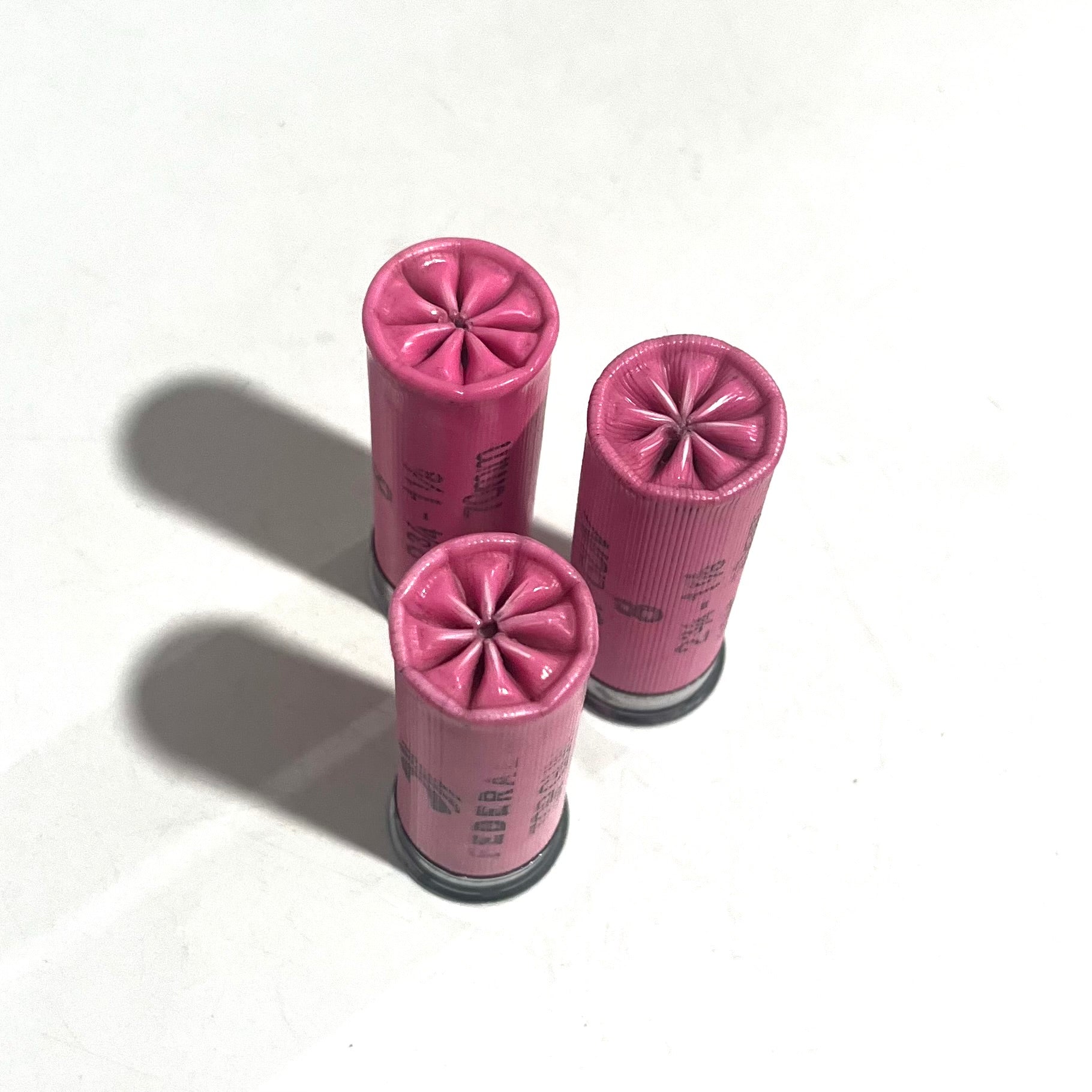 Three pink Federal shotgun shells with fluted star crimp tops on a white background